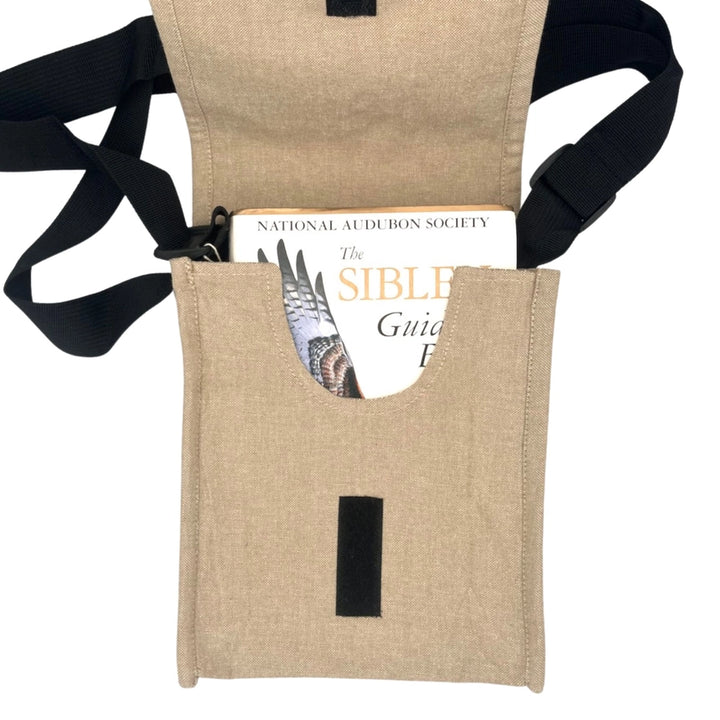 Beige fabric pouch with black strap holding a book titled 'The Sibley Guide to Birds' on a white background
