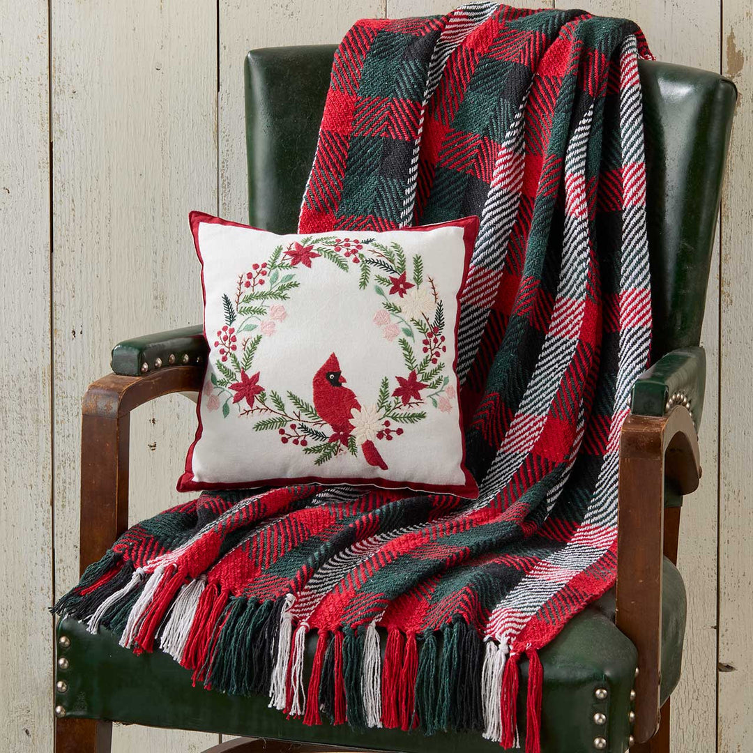 Green chair with a red and green plaid blanket and a decorative pillow featuring a cardinal.