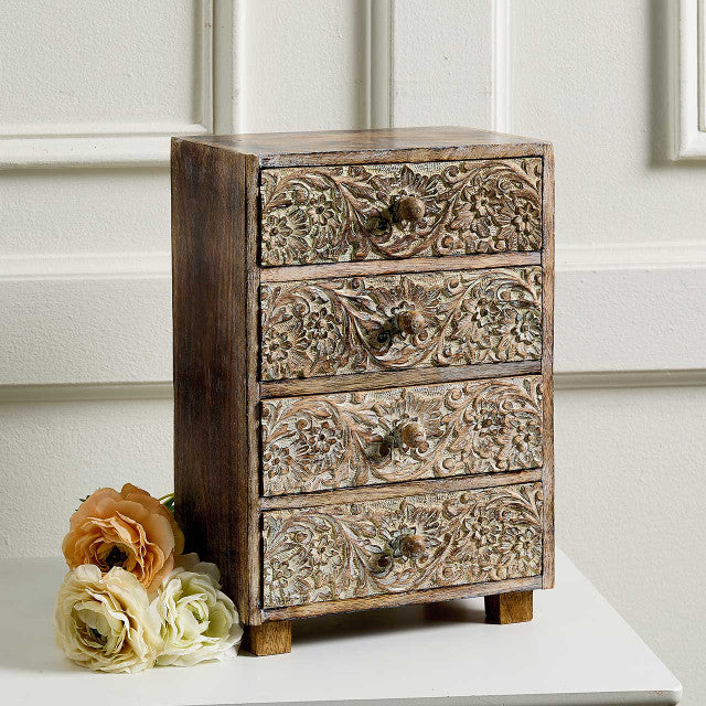 Decorative wooden chest of drawers with floral carvings on a white surface.