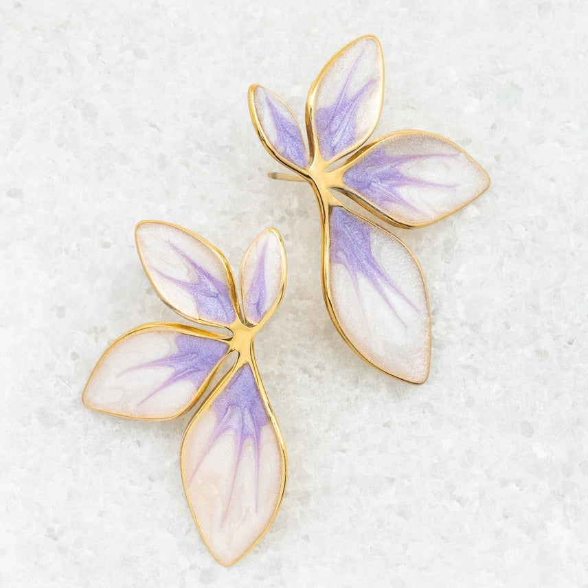 floral-shaped earrings with purple and white wings on a textured white surface