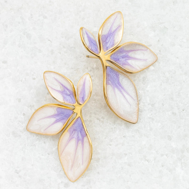 floral-shaped earrings with purple and white wings on a textured white surface