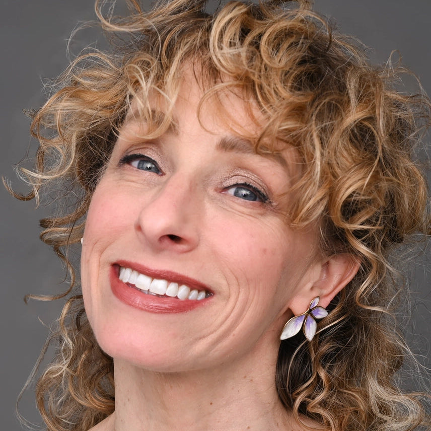 Woman with curly blonde hair wearing earrings against a gray background