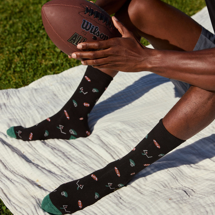 Person wearing black socks with football designs, sitting on a blanket holding a Wilson football.