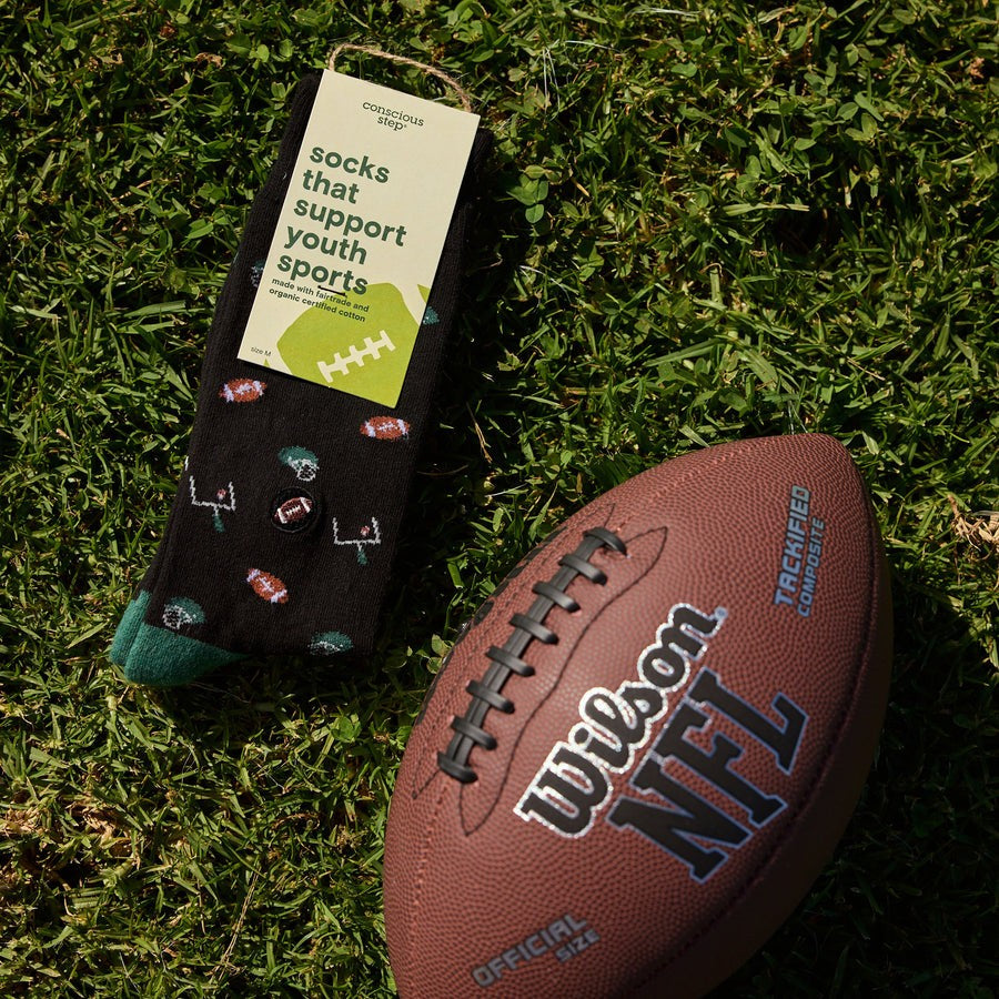 Black socks with sports-themed design on grass next to a Wilson NFL football