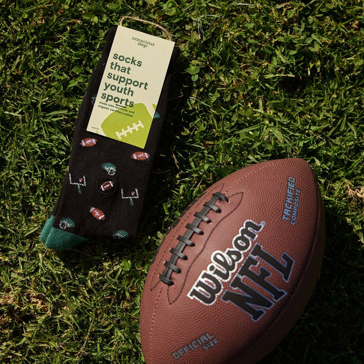 Black socks with sports-themed design on grass next to a Wilson NFL football