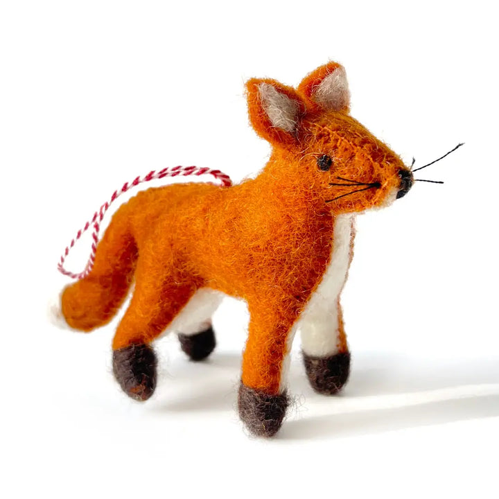 A small felted wool fox ornament in orange, white, and brown, with a red-and-white string tail, photographed on a clean white background.