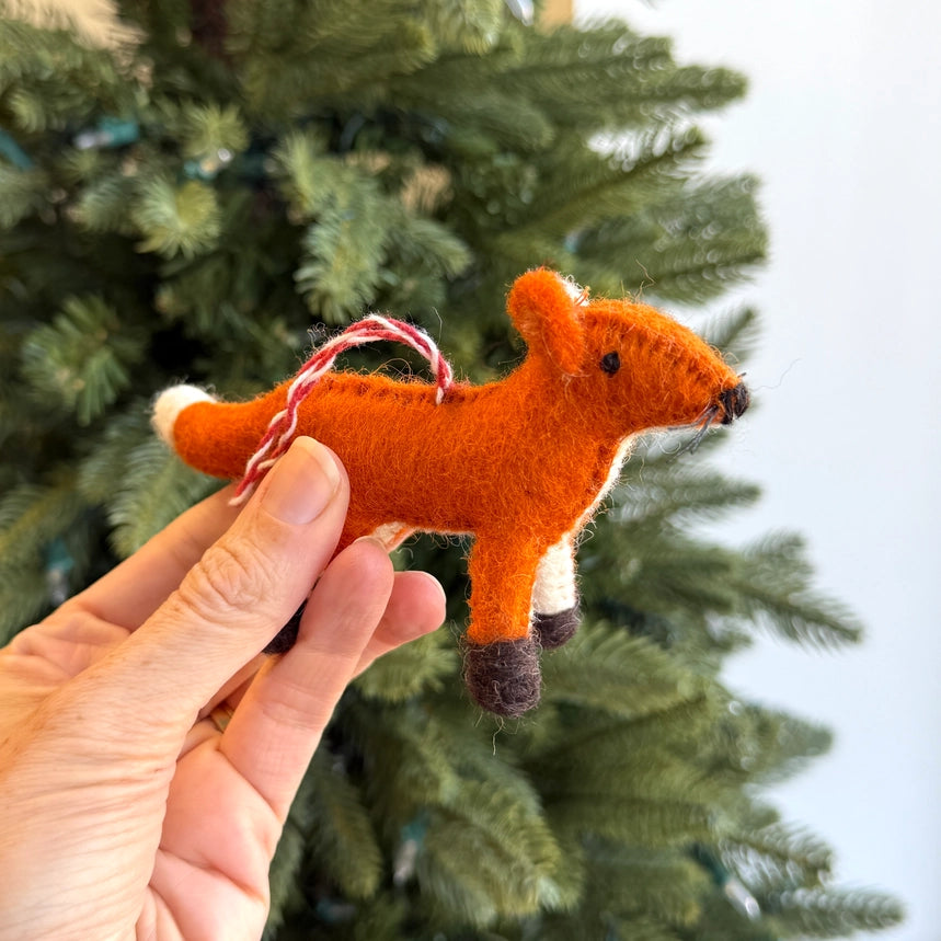 Hand holding a felt fox ornament in front of a Christmas tree.