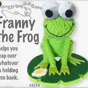 A crocheted green frog sting doll with large white eyes and a stitched smile, sitting on a green lily pad. The image includes text reading 'The string doll game' and 'Granny the Frog' on a white background.