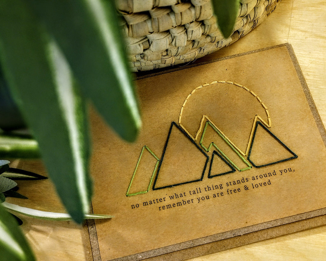 Card with mountain design and text on a wooden surface with plants