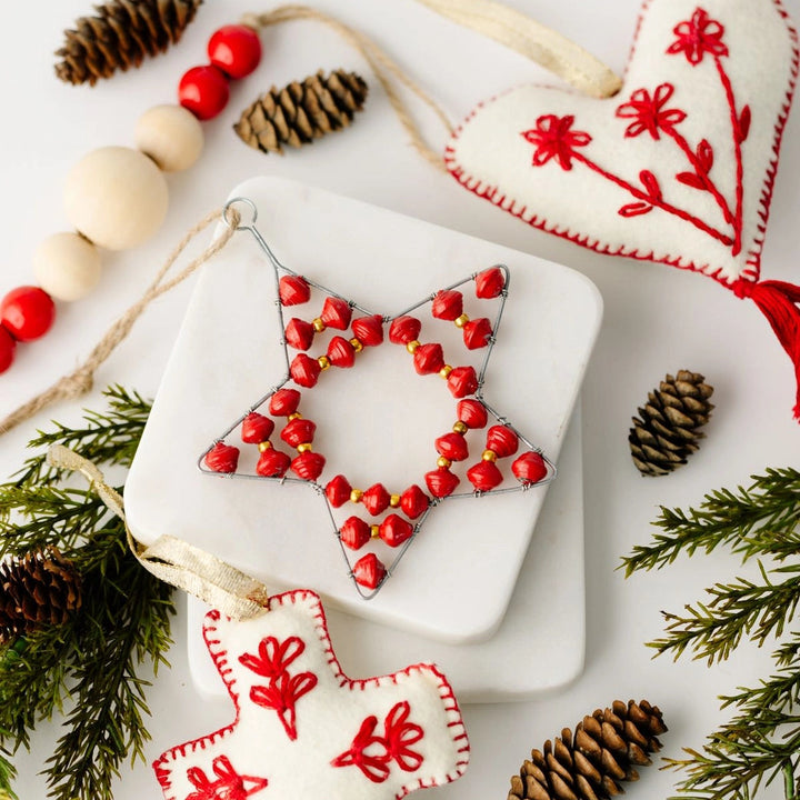 Decorative Christmas ornament with red beads on a white surface with pine cones and greenery.
