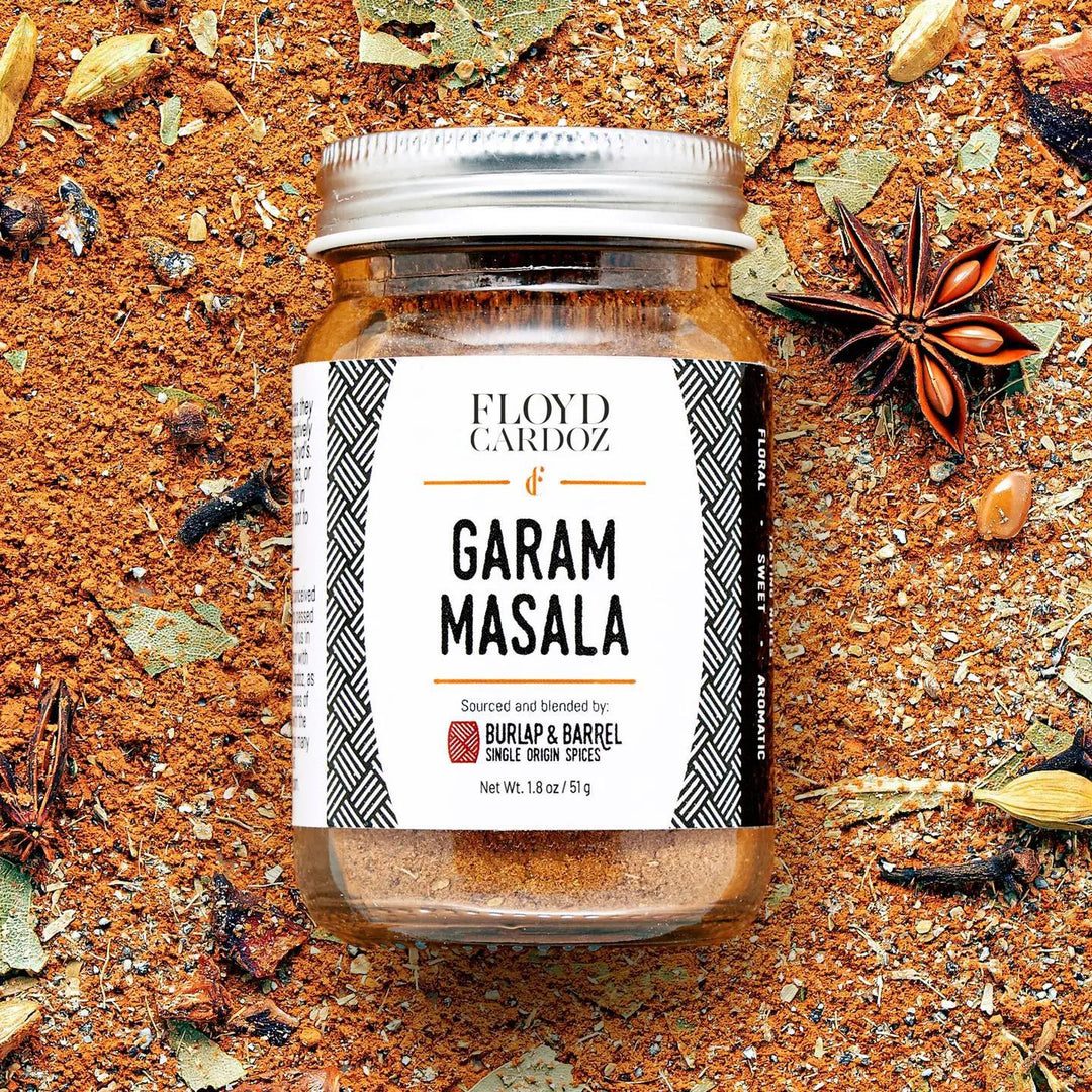 Jar of Floyd Cardoz Garam Masala spice blend on a textured surface with spices around.