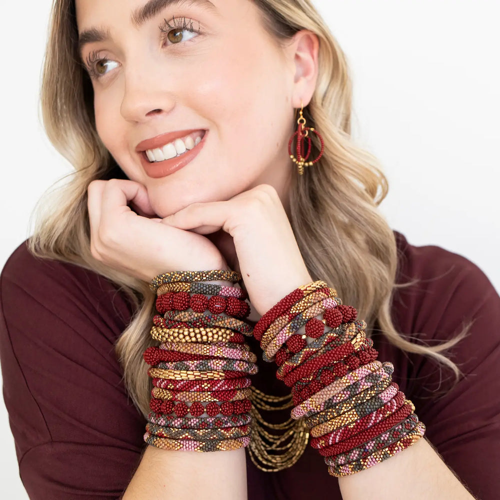 A woman wearing multiple beaded roll on bracelets on both wrists and red hoop earrings, posed against a clean white background.