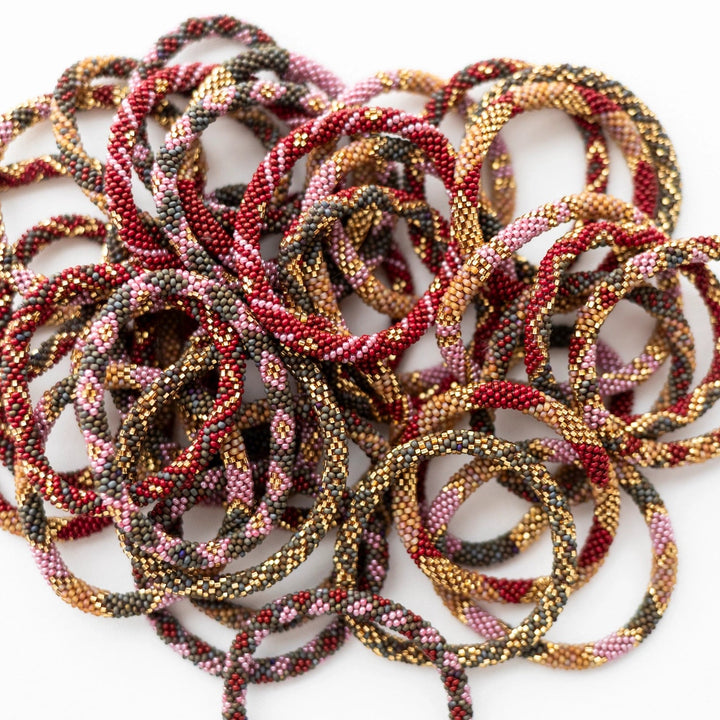 A pile of beaded roll-on bracelets in a multicolor pattern of red, gold, brown, and black, arranged on a plain white background.