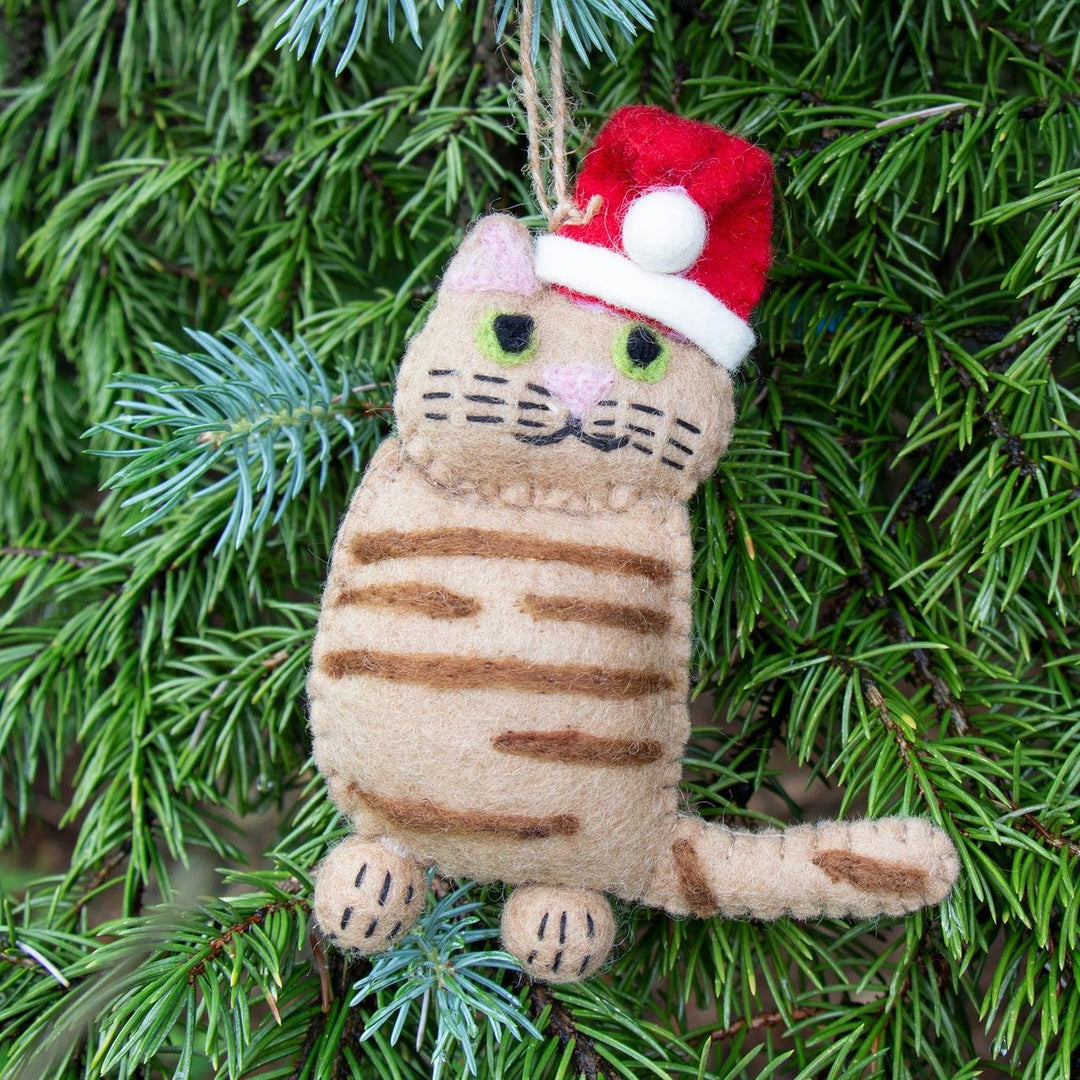 Cat-shaped Christmas ornament with a Santa hat hanging on a green pine branch.