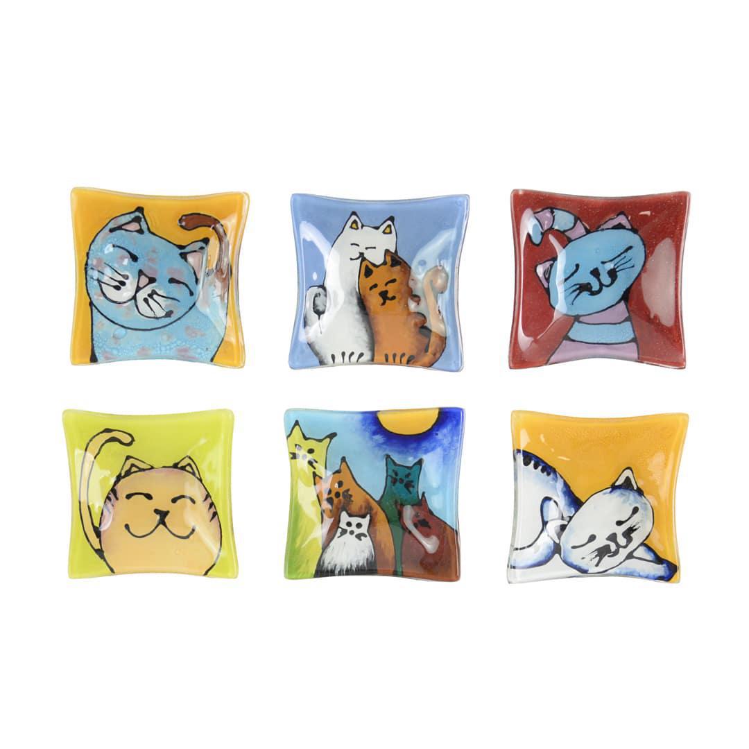 A collection of hand painted glass dishes featuring various smiling cat designs, used for holding small trinkets.