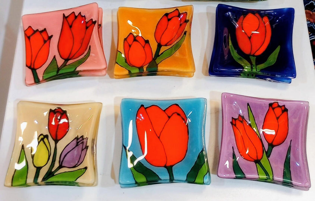 Set of six colorful glass plates with tulip designs on a white surface