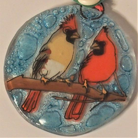 Glass ornament of a cardinal couple on a branch with blue sky