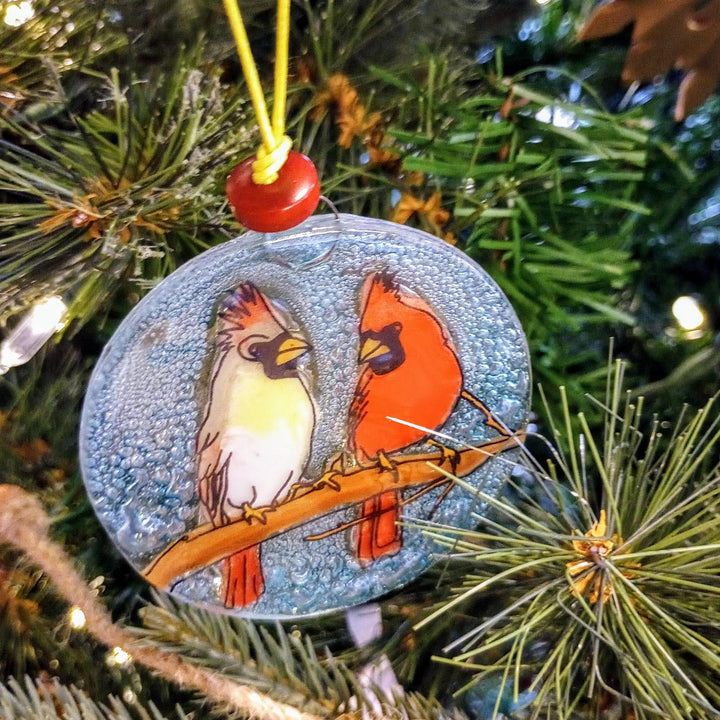 Decorative Christmas ornament with two cardinals on a branch, hanging on a tree.