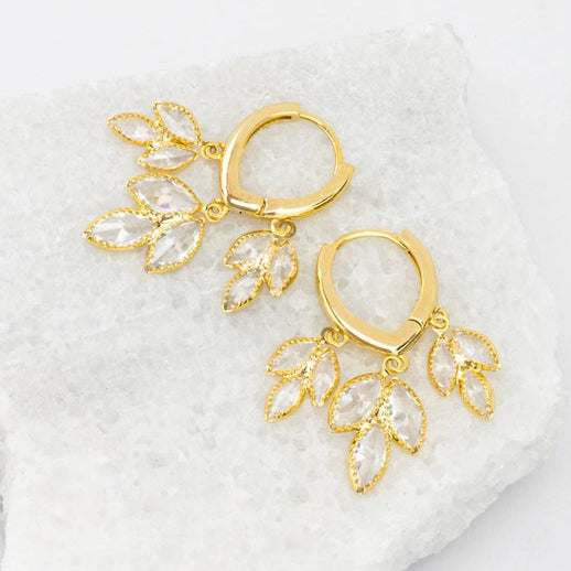 Gold earrings with leaf-like designs on a white stone surface