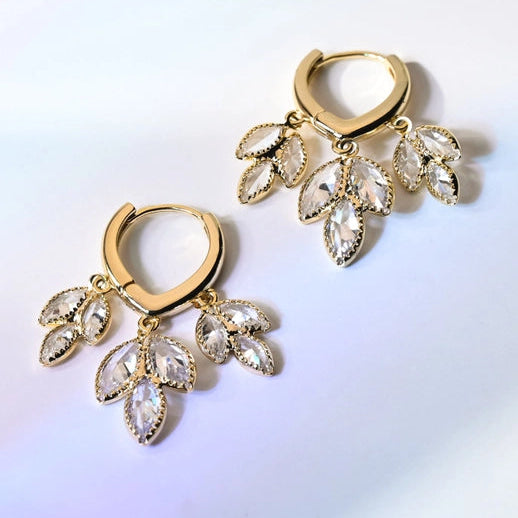 Gold hoop earrings with crystal-like stones on a gradient background