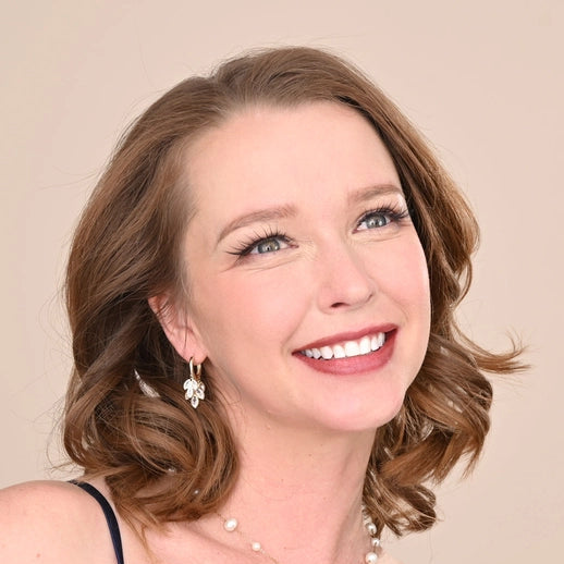 Woman wearing a blue dress with a pearl necklace and earrings against a beige background