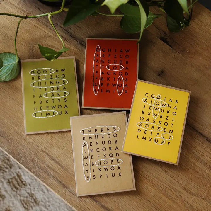 Four crossword themed greeting cards on a wooden table. 