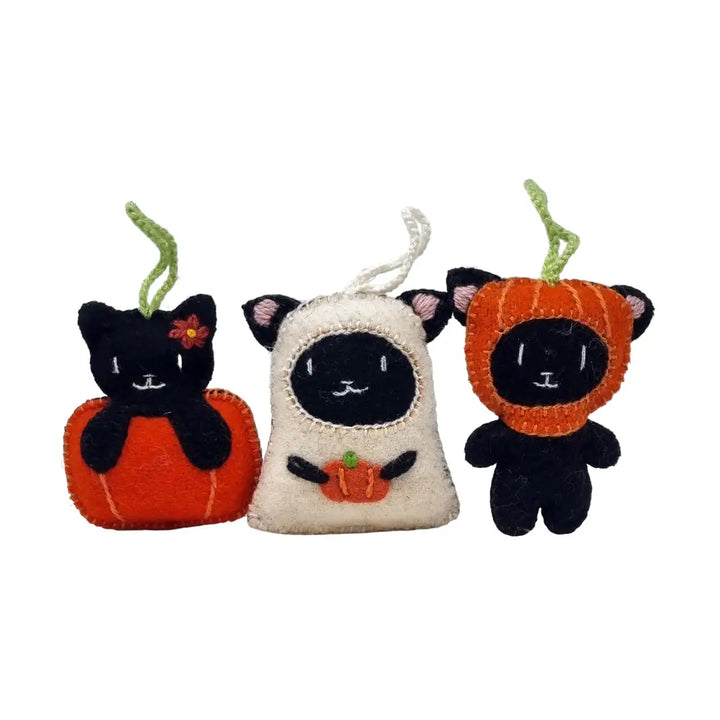 Three handmade felt cat ornaments dressed in Halloween costumes, including a black cat in an orange pumpkin costume, a black cat in a cream sheep costume, and a black cat in an orange pumpkin costume with a green stem.