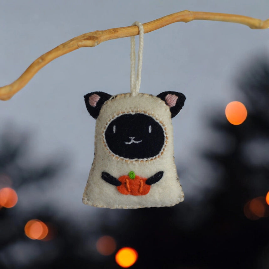 Cat-shaped Halloween ornament hanging from a branch with blurred lights in the background