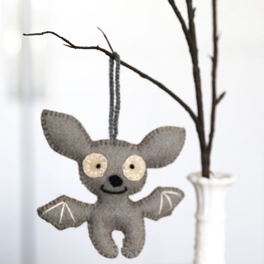 Gray bat-shaped ornament hanging from a branch against a white background