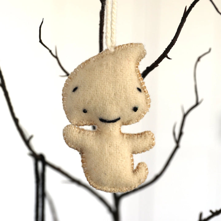 ghost ornament hanging against a white background with tree branches.