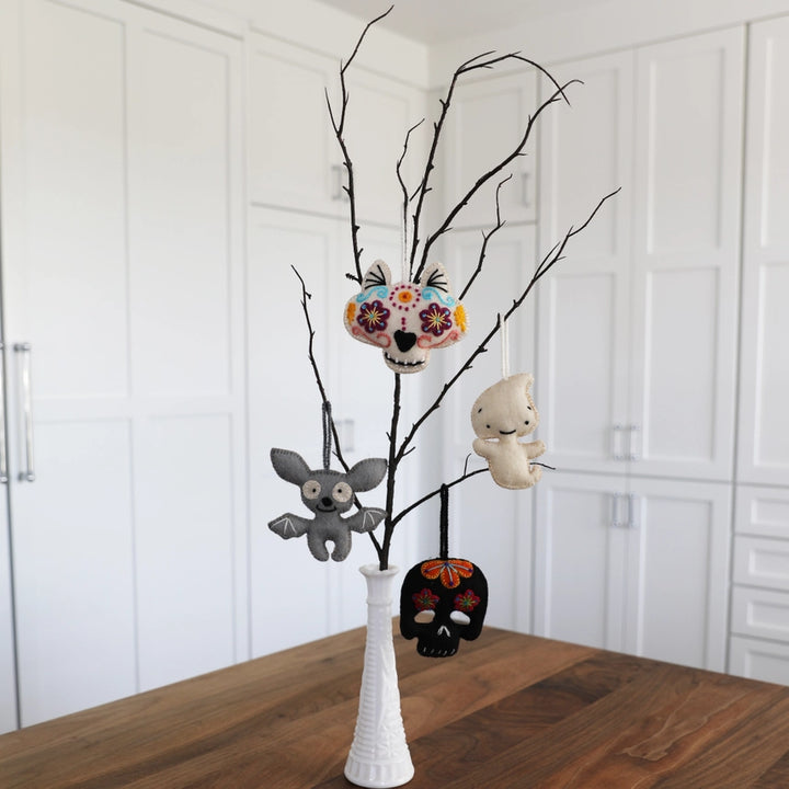 Decorative items including skulls and a ghost on a branch in a white vase against a white wall.
