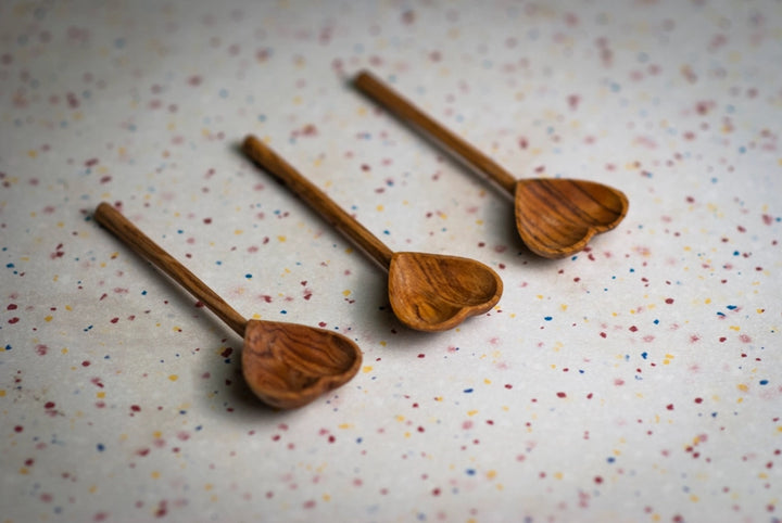 Three wooden heart-shaped spoons on a speckled surface