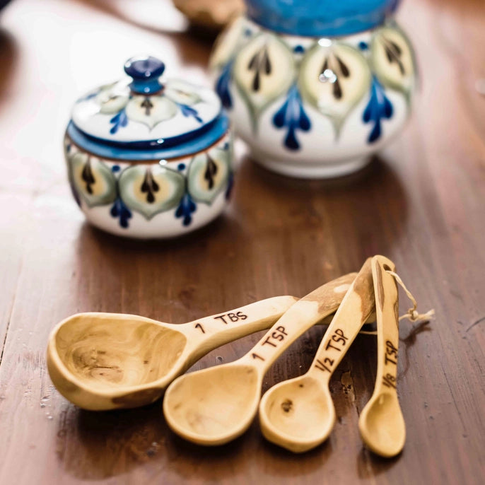 Wooden measuring spoons with ceramic containers on a wooden surface