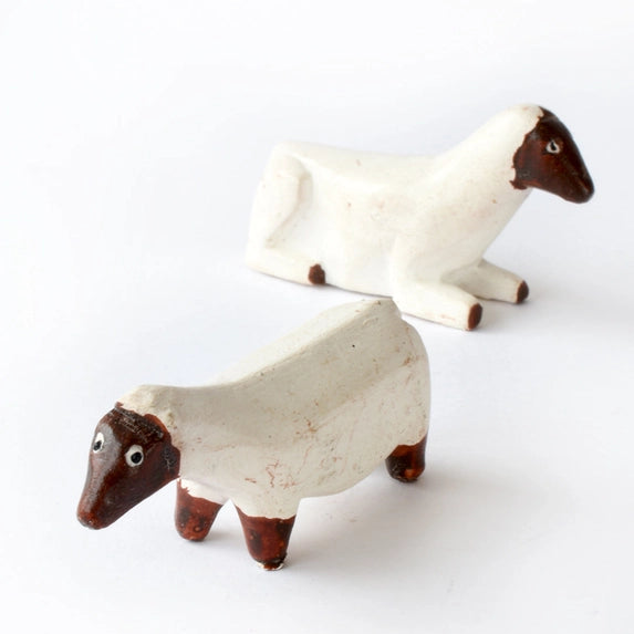 Two small stylized sheep figurines with off-white bodies and dark brown heads and legs, photographed on a plain white background.