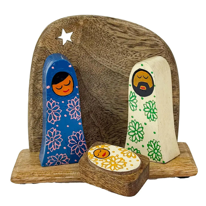 Hand-painted wooden nativity scene figurines on a wooden base, featuring Mary in blue with pink floral patterns, Joseph in cream with green floral patterns, and a small manger box with a yellow patterned lid.