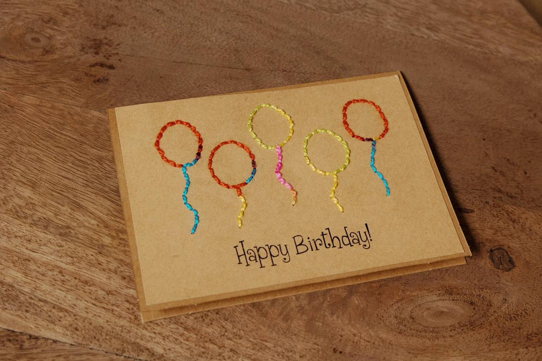 Handmade birthday card with embroidered balloons on a wooden surface