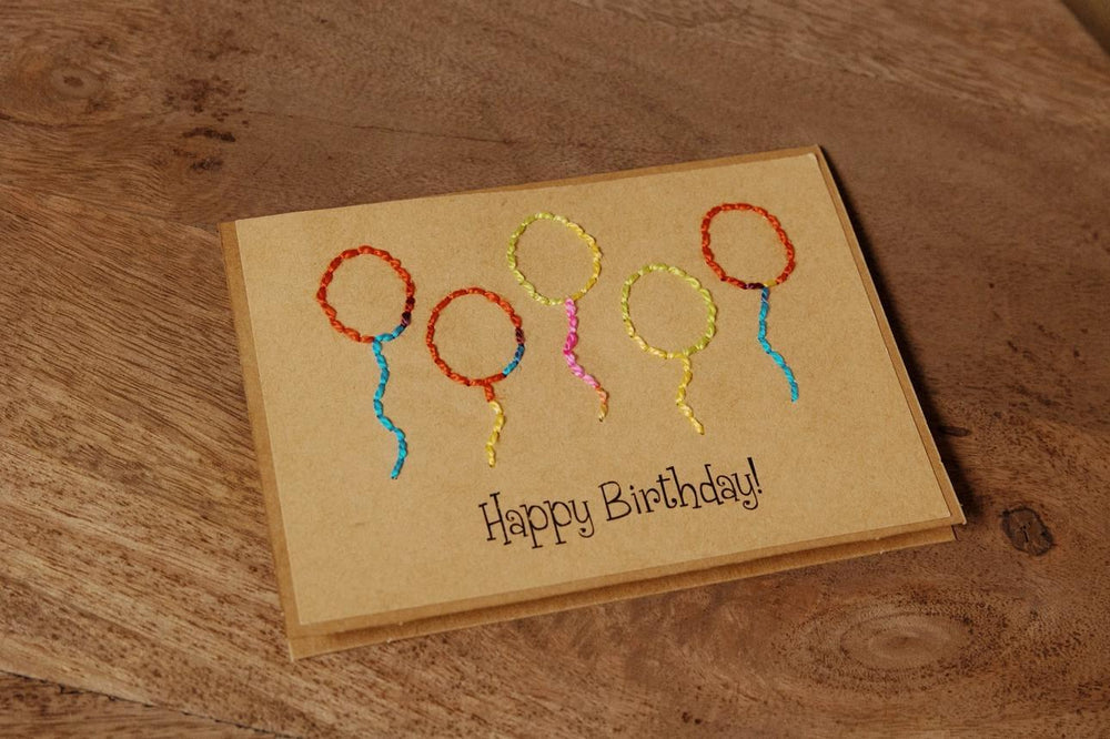 Handmade birthday card with embroidered balloons on a wooden surface