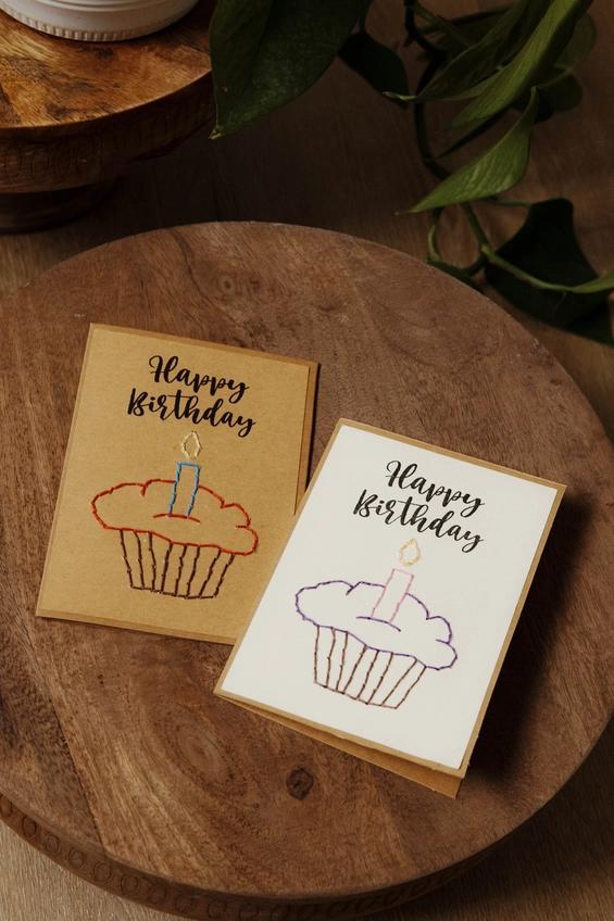 Two 'Happy Birthday' cards with cupcake illustrations on a wooden surface.