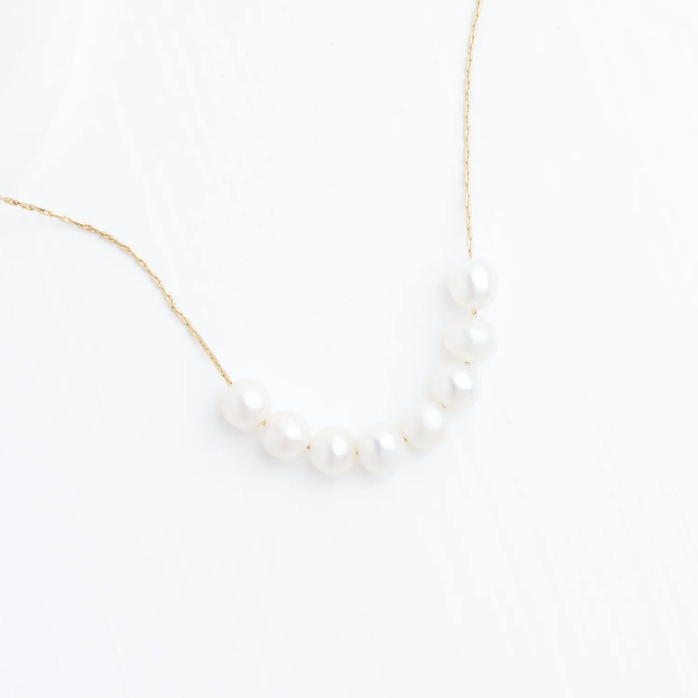 Pearl necklace on a thin gold chain against a white background