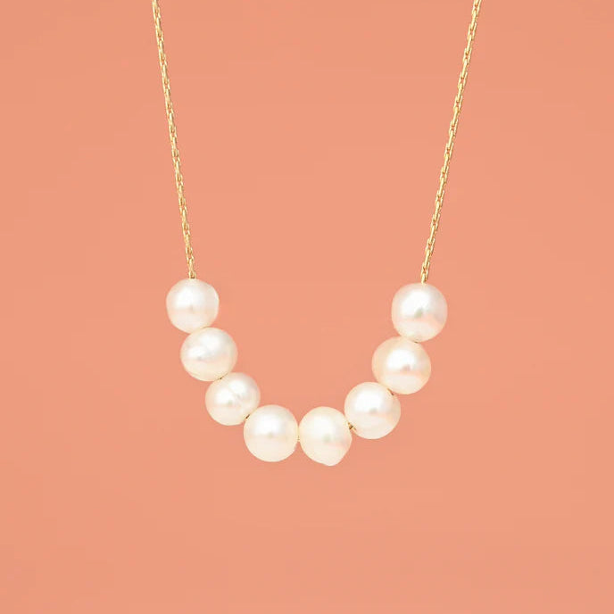 Pearl necklace on a gold chain against a coral background
