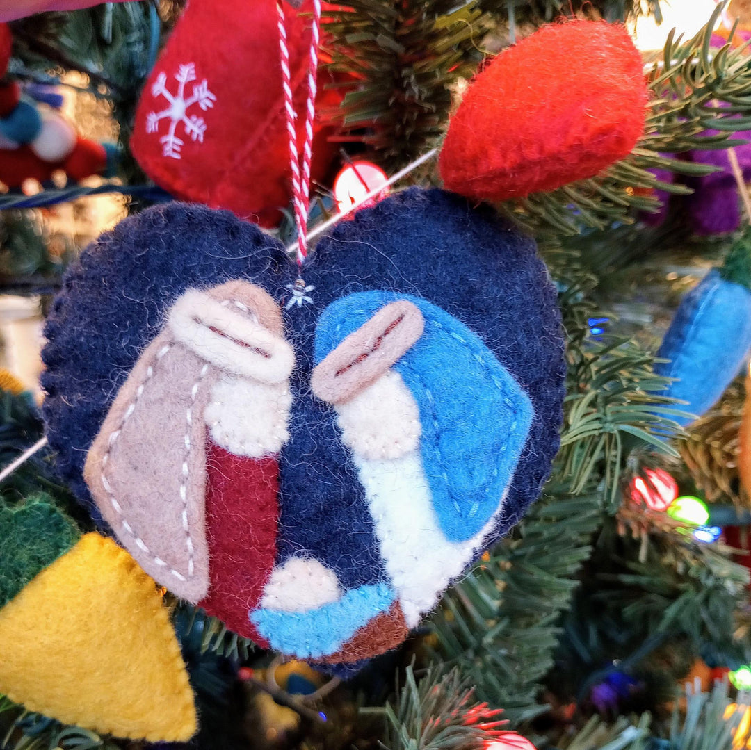a heart nativity felted ornament with a Christmas tree background