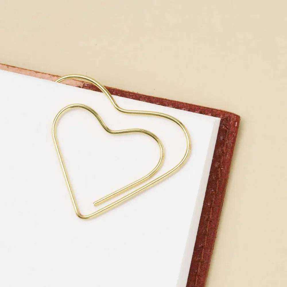 Gold heart-shaped paper clip on a white surface with a beige background