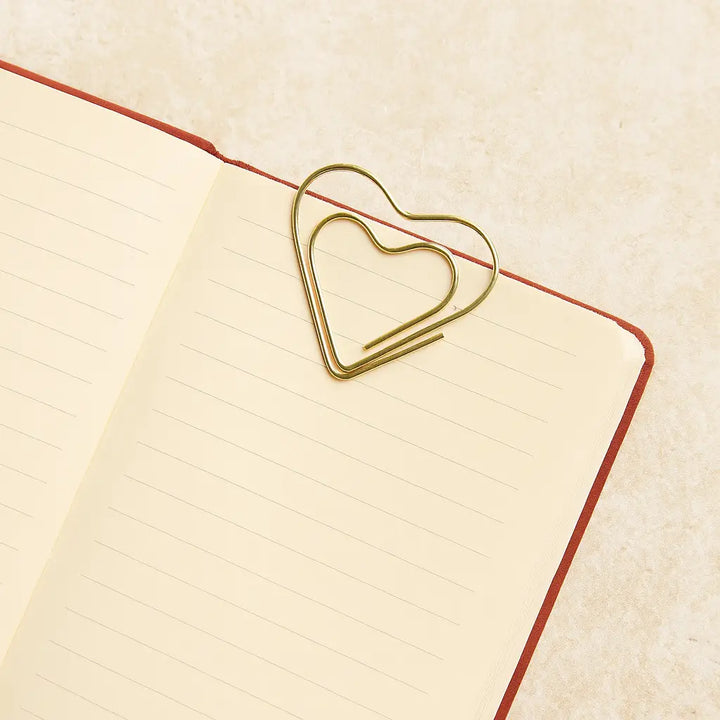 Heart-shaped gold paper clip on a lined notebook page with a beige background
