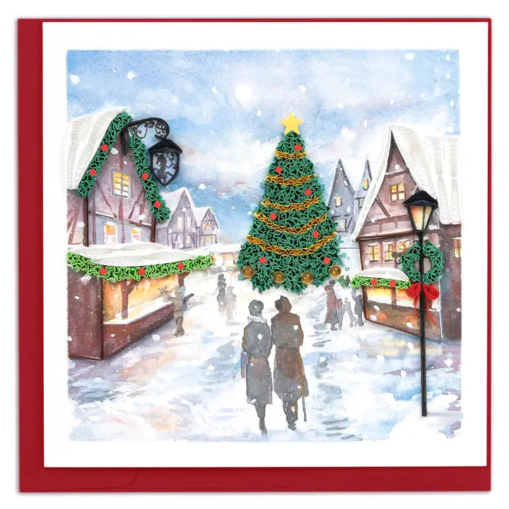 A square Christmas greeting card or art print featuring a snowy village street scene with a decorated Christmas tree, market stalls, lampposts, and two silhouetted figures walking in the snow. The artwork is framed by a white border and a red border.