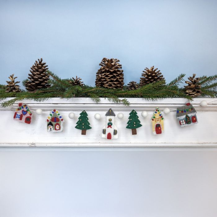 Decorative mantel with pinecones, greenery, and small houses on a light blue background