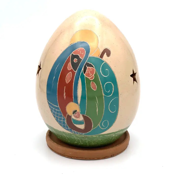 A ceramic nativity egg on a small round wooden base, featuring a colorful painted scene with Mary, Joseph, and baby Jesus, set against a plain white background.