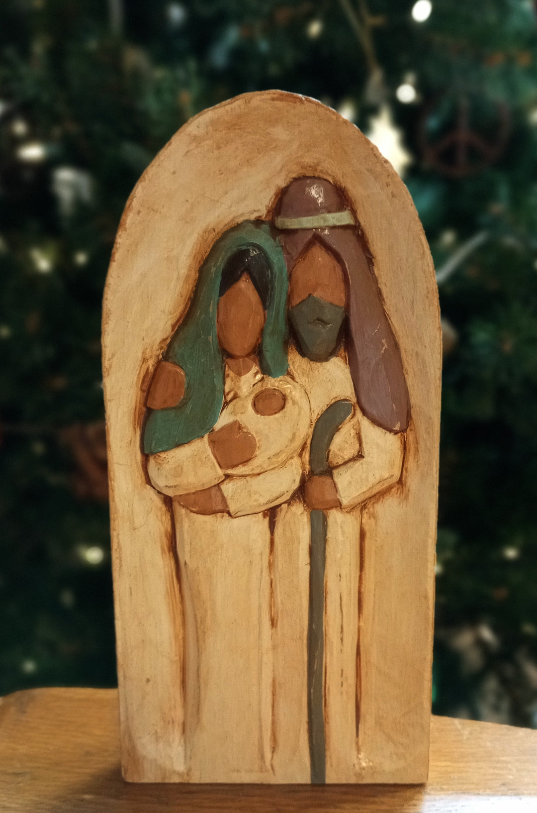 Wooden nativity scene figurine with two figures and a baby, against a blurred green background.