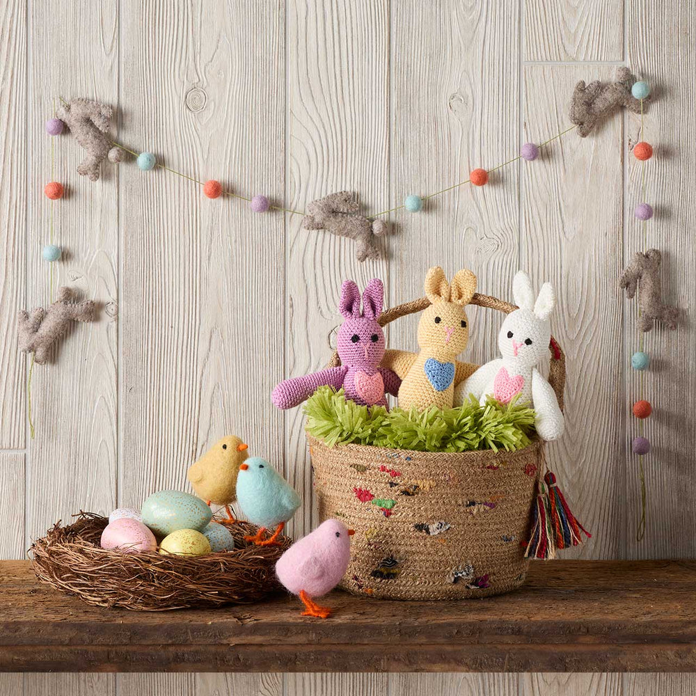 Decorative setup with knitted animals, eggs, and a basket on a wooden surface.