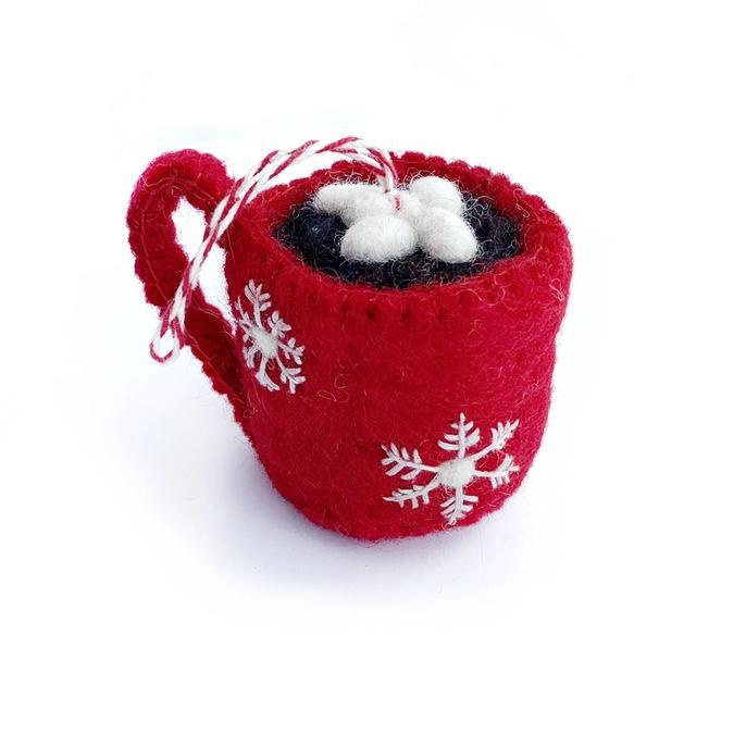 A handcrafted red felt wool ornament shaped like a mug with marshmallows and a white snowflake design on it, with a white ribbon hanging at the top.