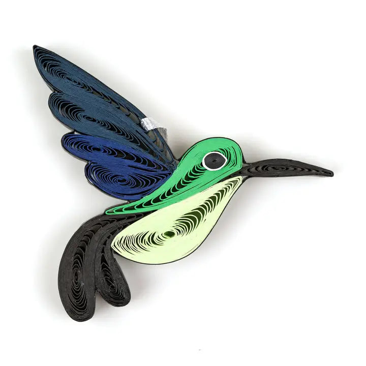 A quilled bird ornament, shaped like a hummingbird, featuring a green head, black beak and tail, blue wings, and a pale yellow underbelly, set against a plain white background.